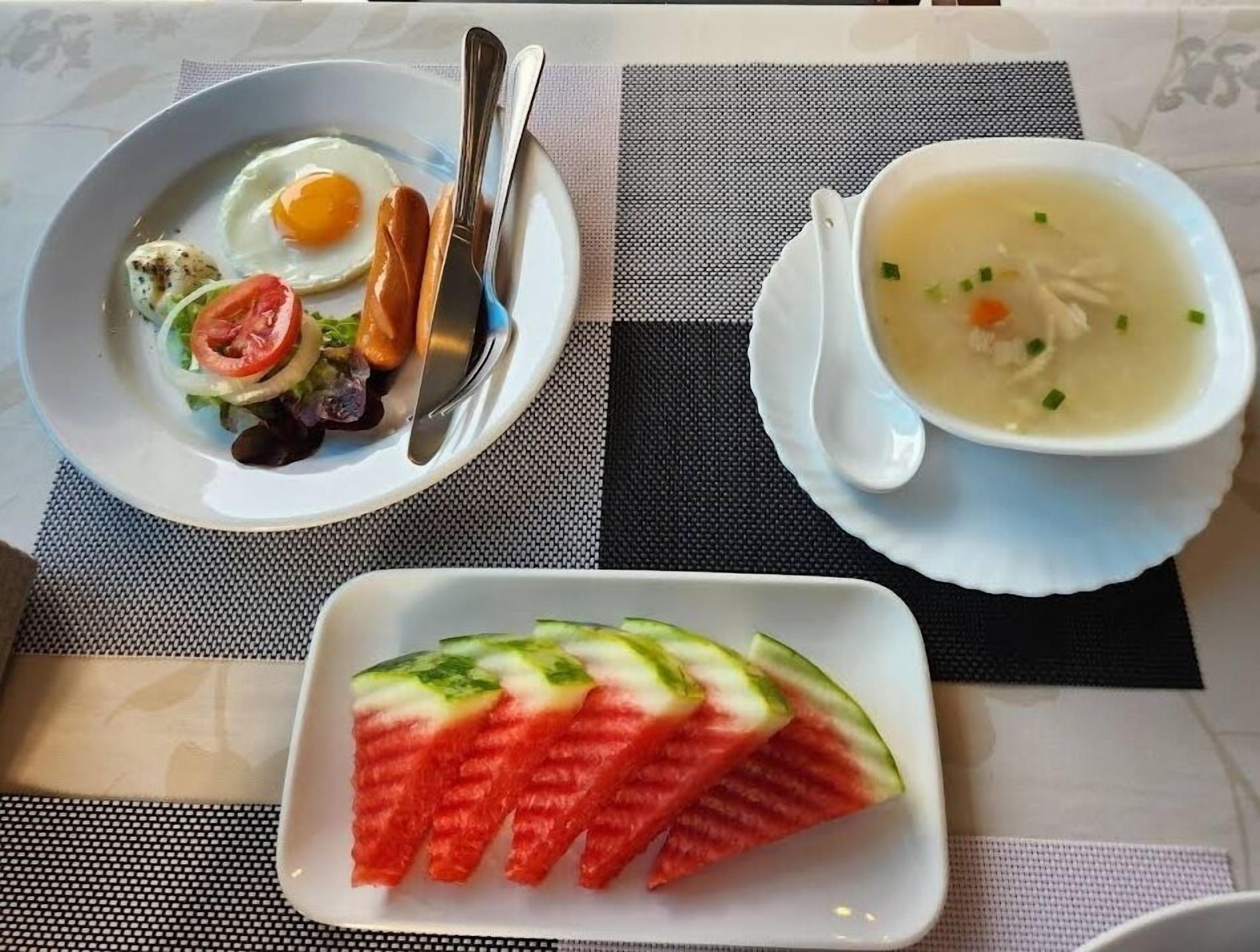 A breakfast setting with a plate of eggs, toast, and salad, a bowl of soup, and a plate of watermelon slices.