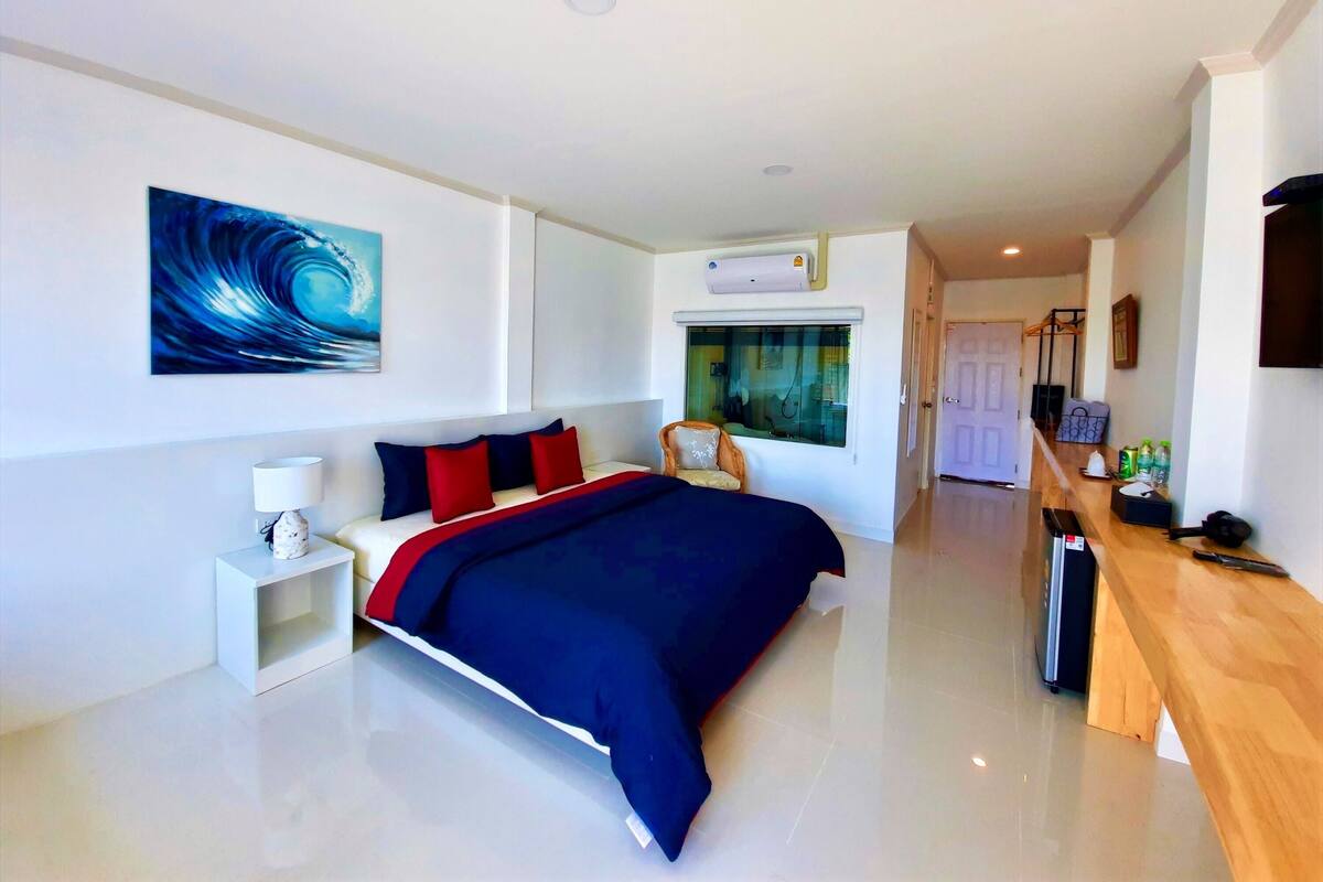 A modern hotel room with a large bed, a bedside table, a TV, and a window with a view.