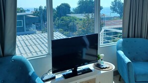 A modern living room with a large window, a flat-screen TV, and two blue armchairs. - Koh Larn Riviera (Koh Lan)