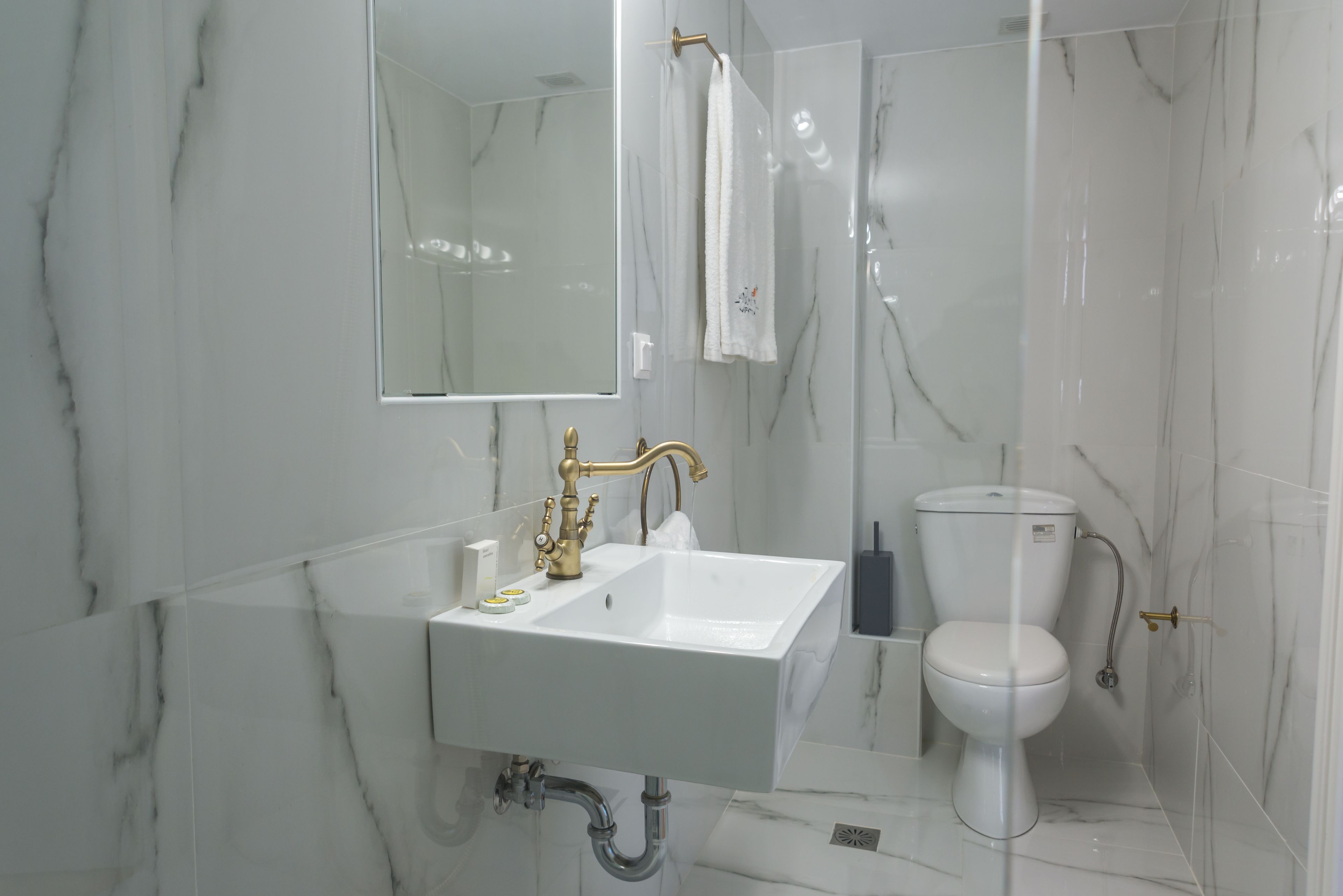 Et badeværelse med en hvid vask, guldfarvet armatur og et toilet.