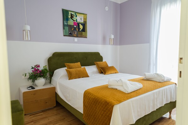 A neatly made bed with a green headboard, a bedside table with a vase of flowers, and a painting on the wall.