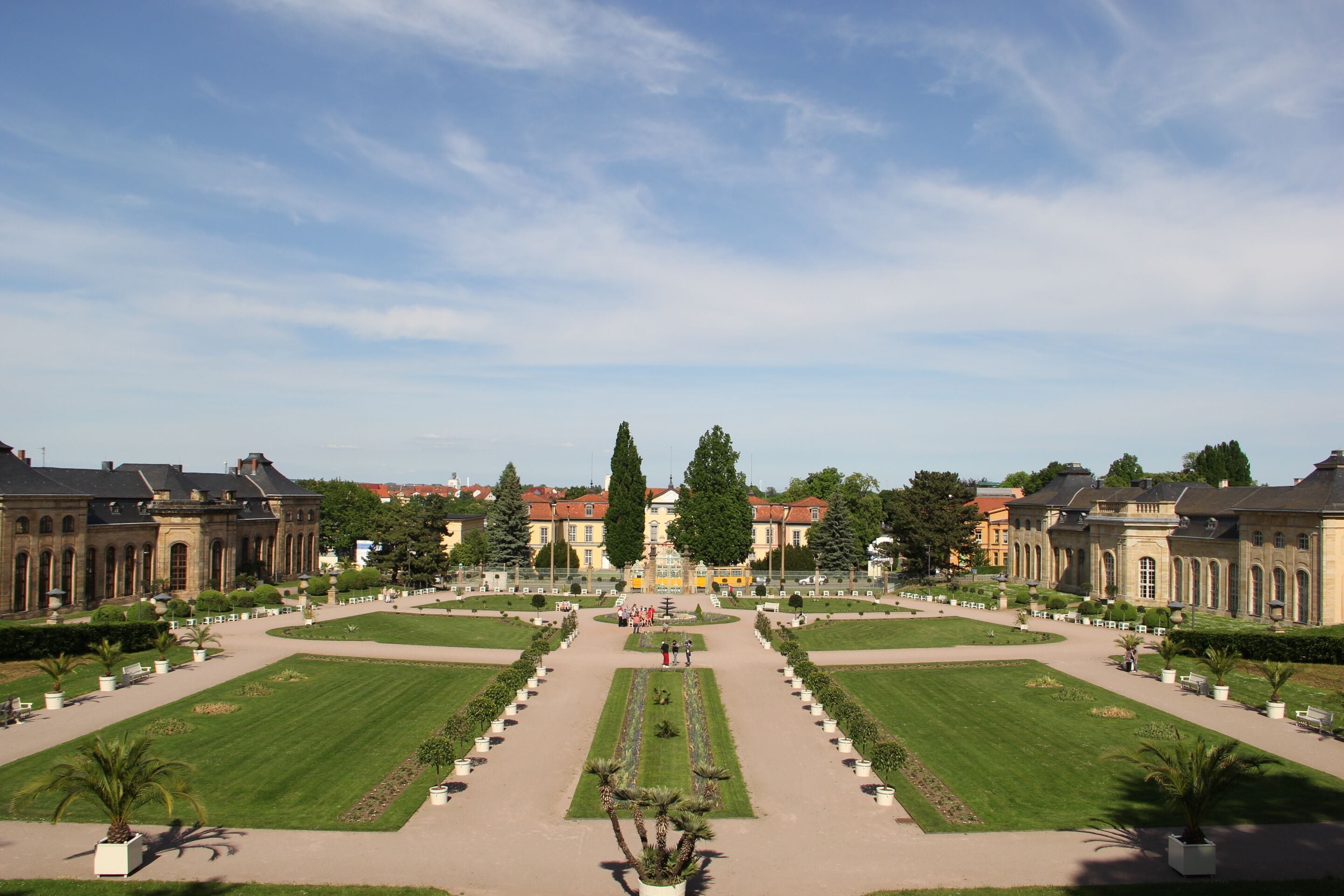 Un jardín simétrico con una fuente central, rodeado de céspedes cuidados y arquitectura clásica.