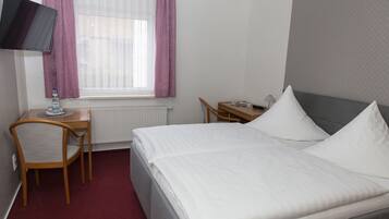 A hotel room with a bed, a desk, a chair, a television, and a window with curtains.