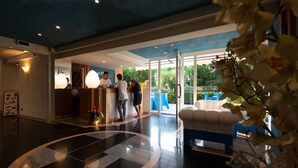 Un vestíbulo de hotel con un mostrador de recepción, una zona de estar con sofá y un amplio ventanal que ofrece vistas al exterior.