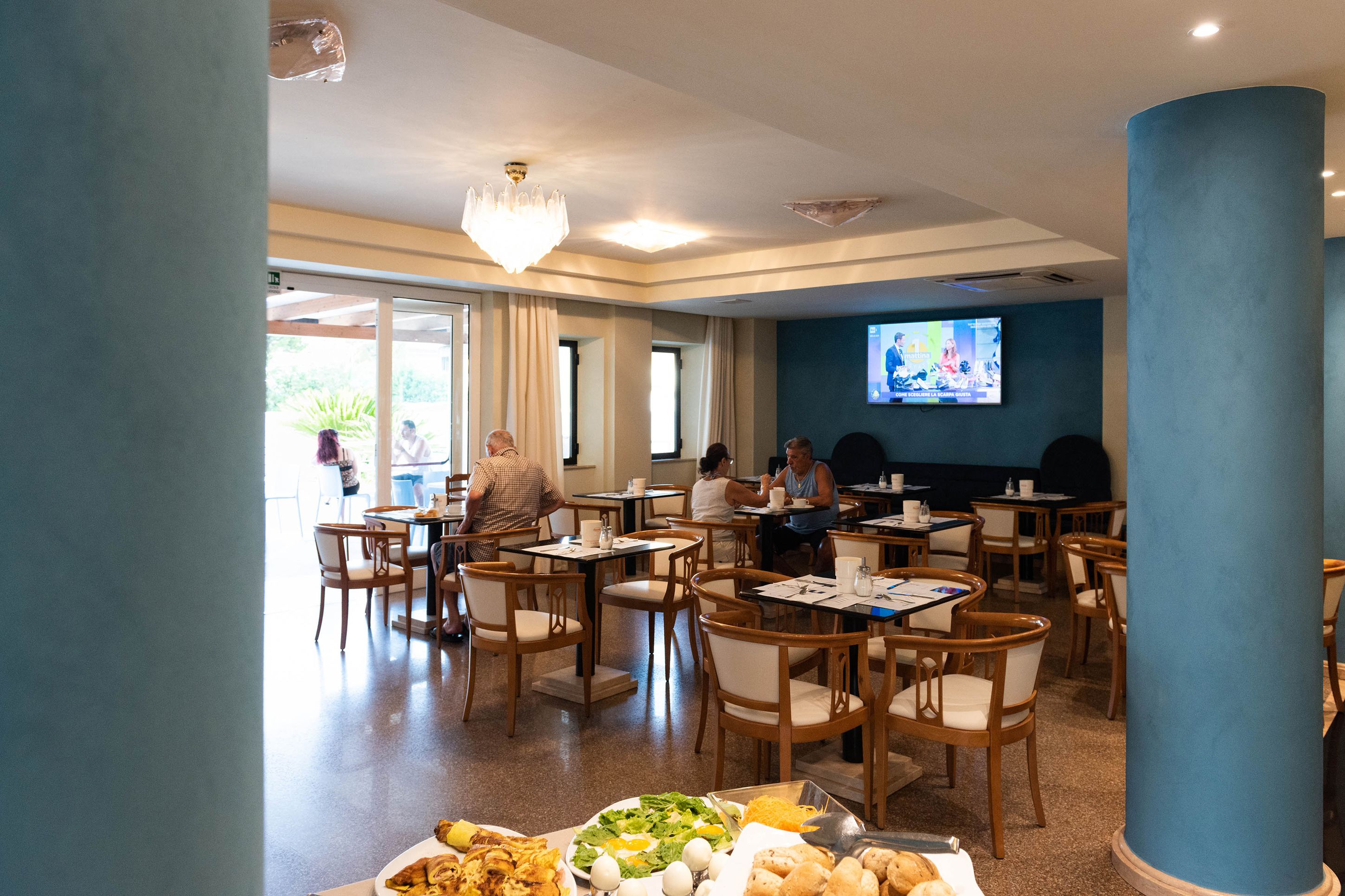 A dining area with tables and chairs, a buffet with various food items, and a television screen displaying a program.