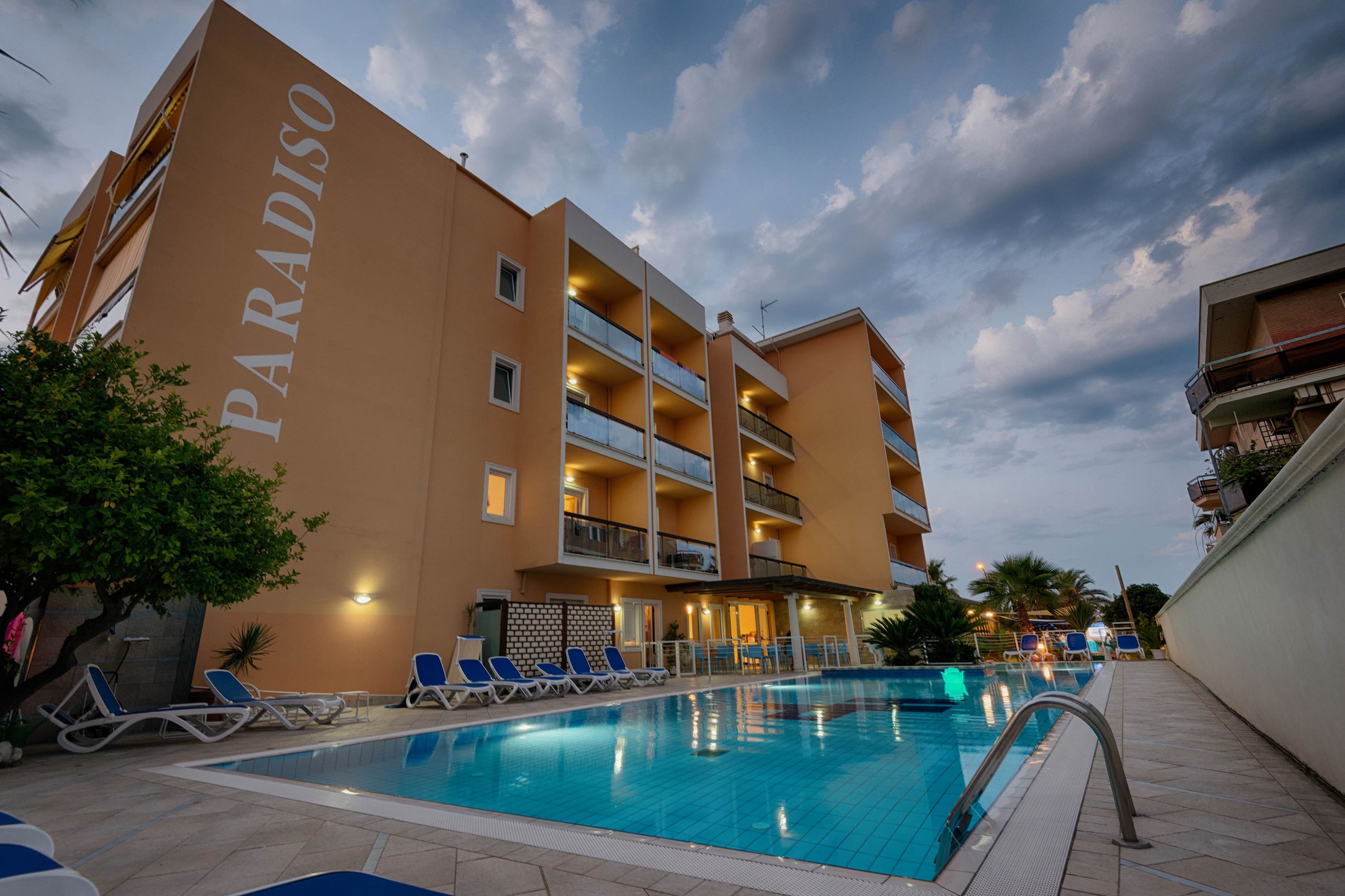 Hotel PARADISO met een zwembad, ligbedden en een heldere lucht.