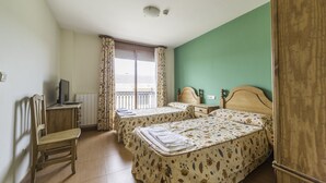 Quarto com duas camas, uma escrivaninha com computador, uma cadeira e uma janela com cortinas.