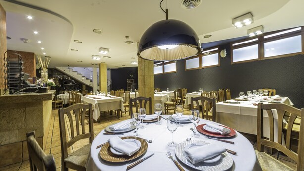 Restaurante com mesas redondas preparadas para refeições, com toalhas brancas, pratos dourados e prateados, e guardanapos dobrados com cuidado.
