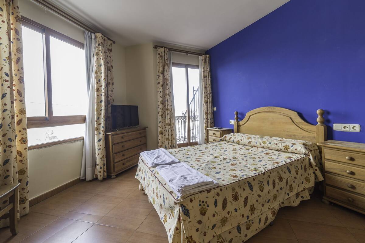 Un dormitorio con cama, cómoda, mesita de noche y televisor sobre la cómoda.