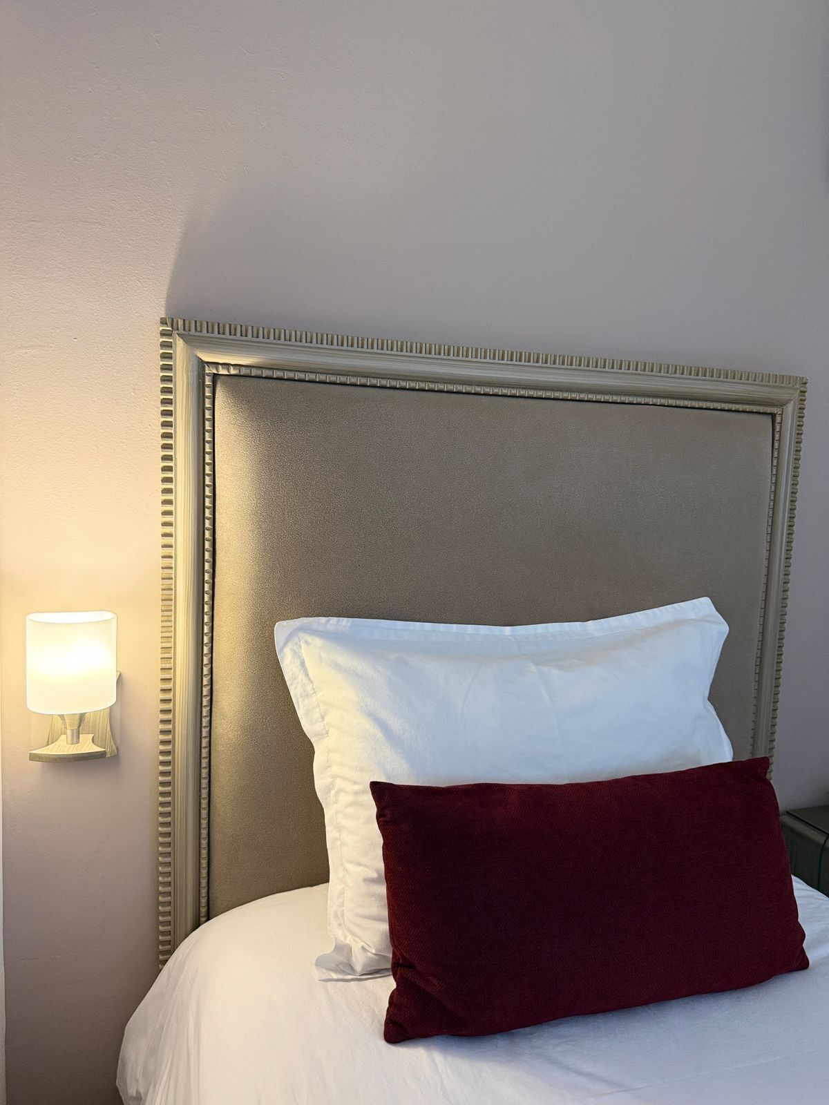 A bed with a headboard, a white pillow, a red pillow, and a wall-mounted light.