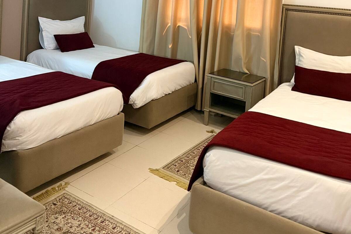 Quarto de hotel com duas camas, mesa de cabeceira, cadeira e janela com cortinas.