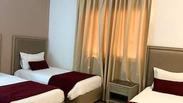 Habitación de hotel con dos camas, una mesita de noche, una silla y un ventanal con cortinas.
