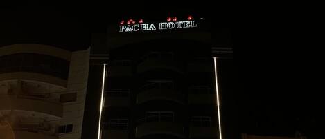 A multi-story hotel with a prominent sign at the top, a glass entrance, and several parked cars in front.