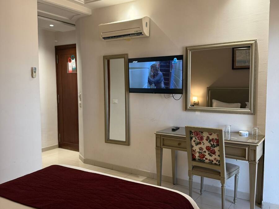 Habitación de hotel con cama, escritorio con silla, televisión, espejo y aire acondicionado.
