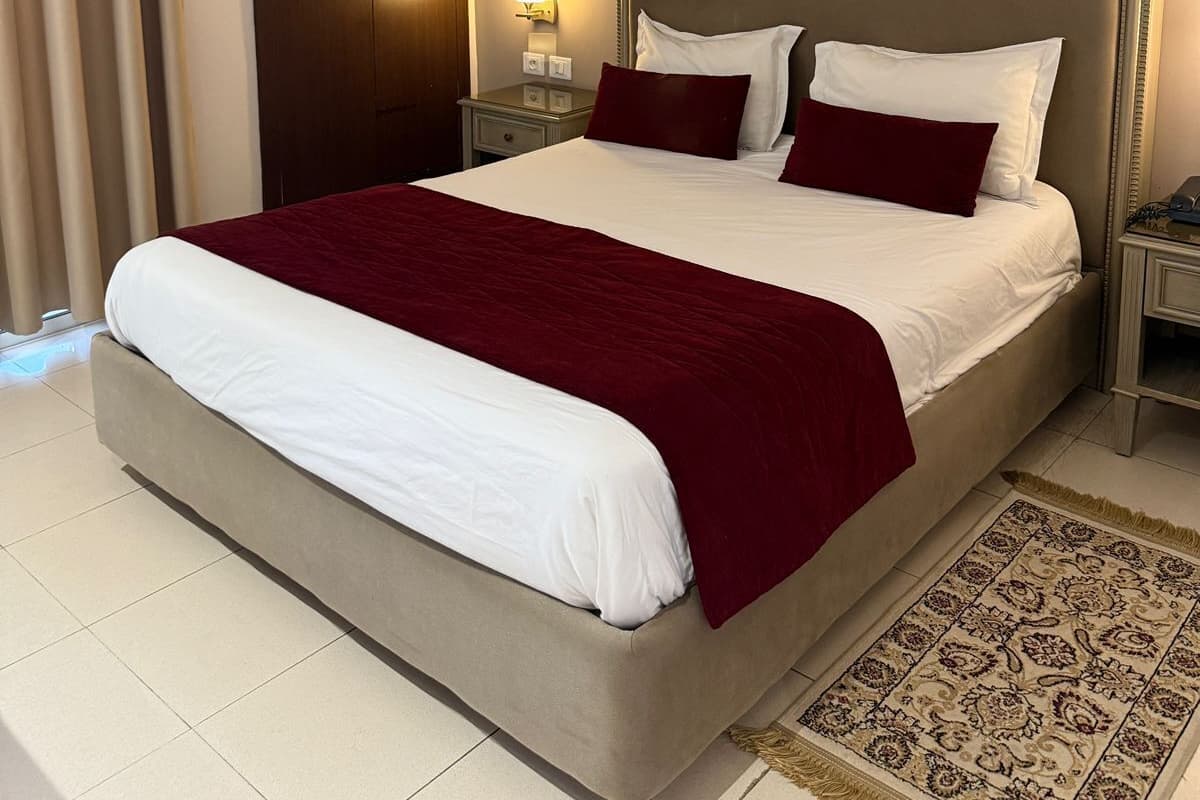 Quarto de hotel com uma cama grande, um guarda-roupa, uma mesa de cabeceira, um abajur e um quadro na parede.