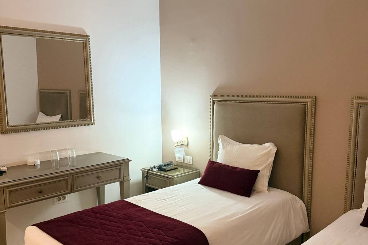Quarto de hotel com duas camas, uma mesa, um espelho e uma mesa de cabeceira com abajur.