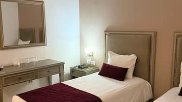 A hotel room with two beds, a desk, a mirror, and a nightstand with a lamp.