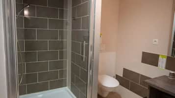 A bathroom with a glass-enclosed shower, a toilet, and a sink area.