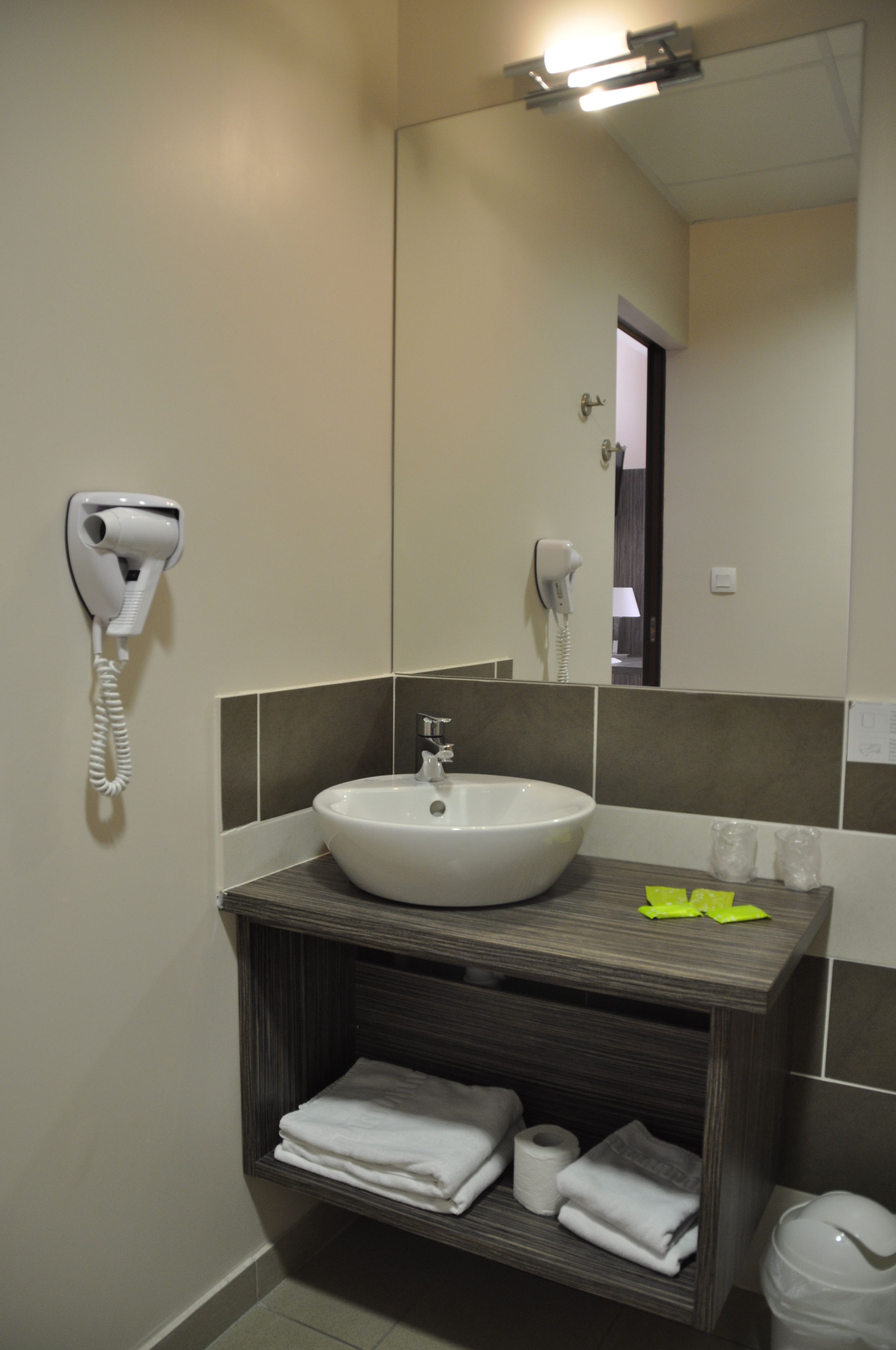 A bathroom with a sink, a hairdryer, a mirror, and a shelf with towels.