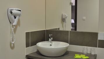 A bathroom with a sink, a hairdryer, a mirror, and a shelf with towels.