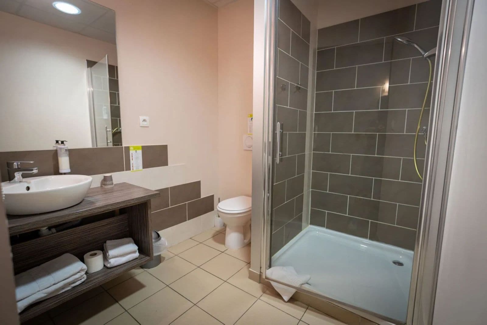 Un baño con lavamanos, espejo, inodoro y cabina de ducha con paredes de vidrio.