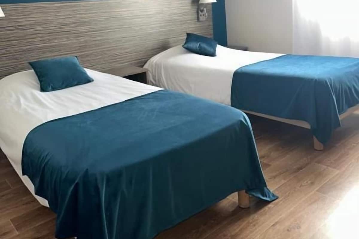 A hotel room with two beds, each with a blue bedspread and white linens.