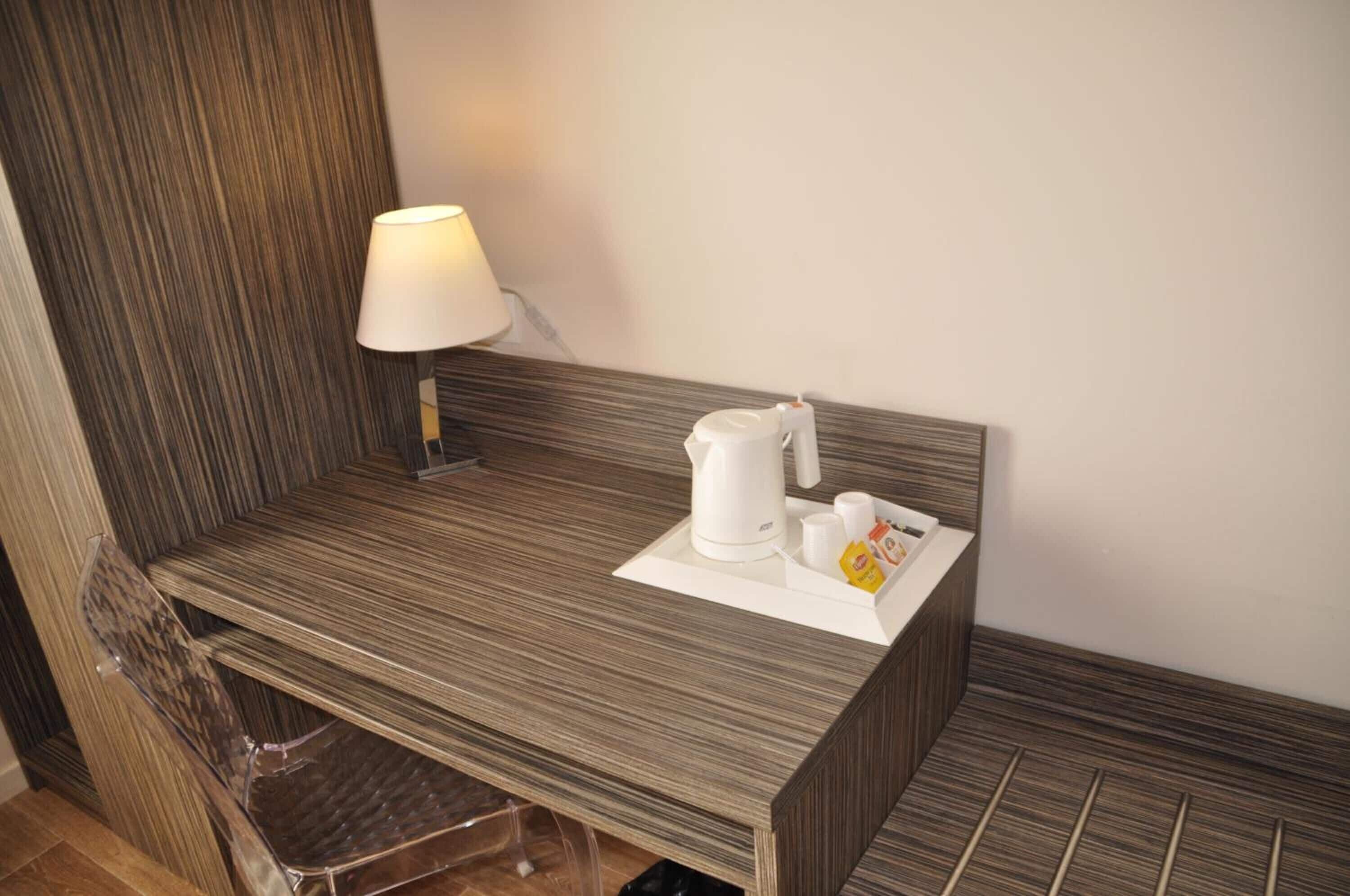 A small, modern kitchenette with a wooden countertop, a kettle, cups, and a tea bag holder.