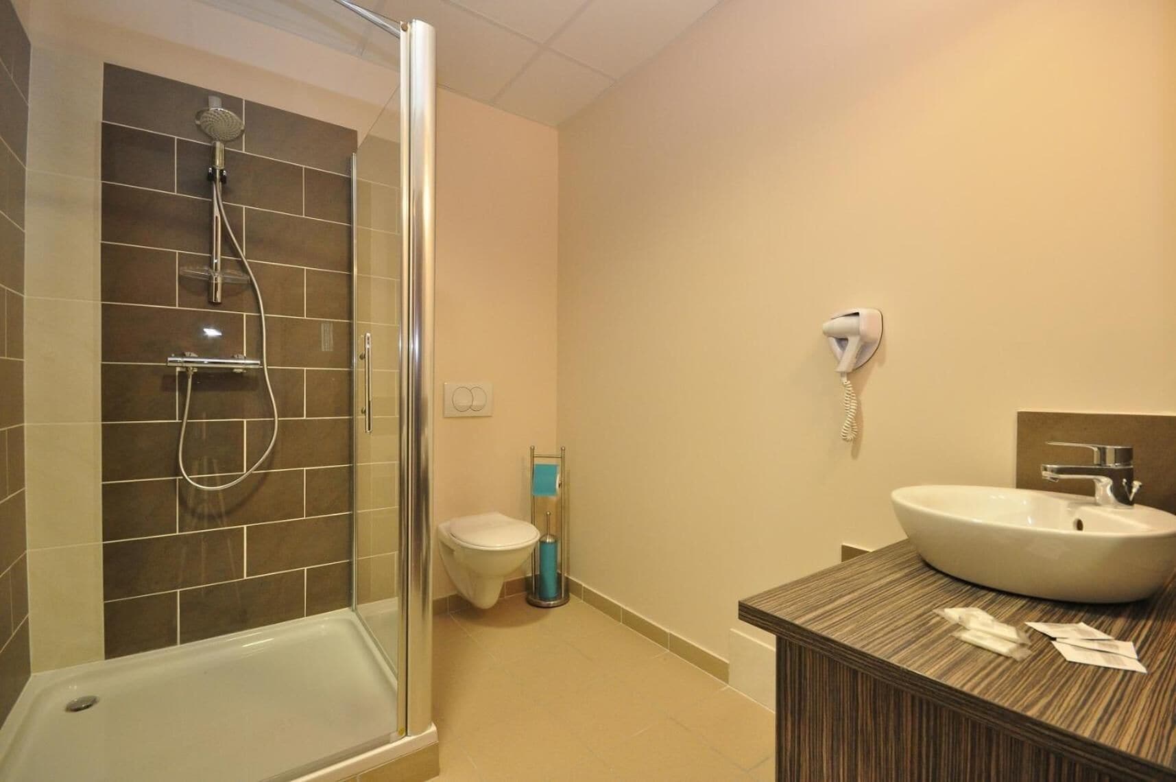 Un baño con ducha de vidrio, inodoro y lavamanos con encimera de madera.