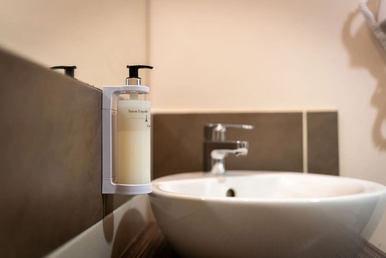 A bathroom with a white sink and a soap dispenser mounted on the wall.