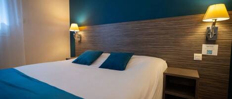 A hotel room with a large bed, two pillows, a nightstand, and wall-mounted lamps.