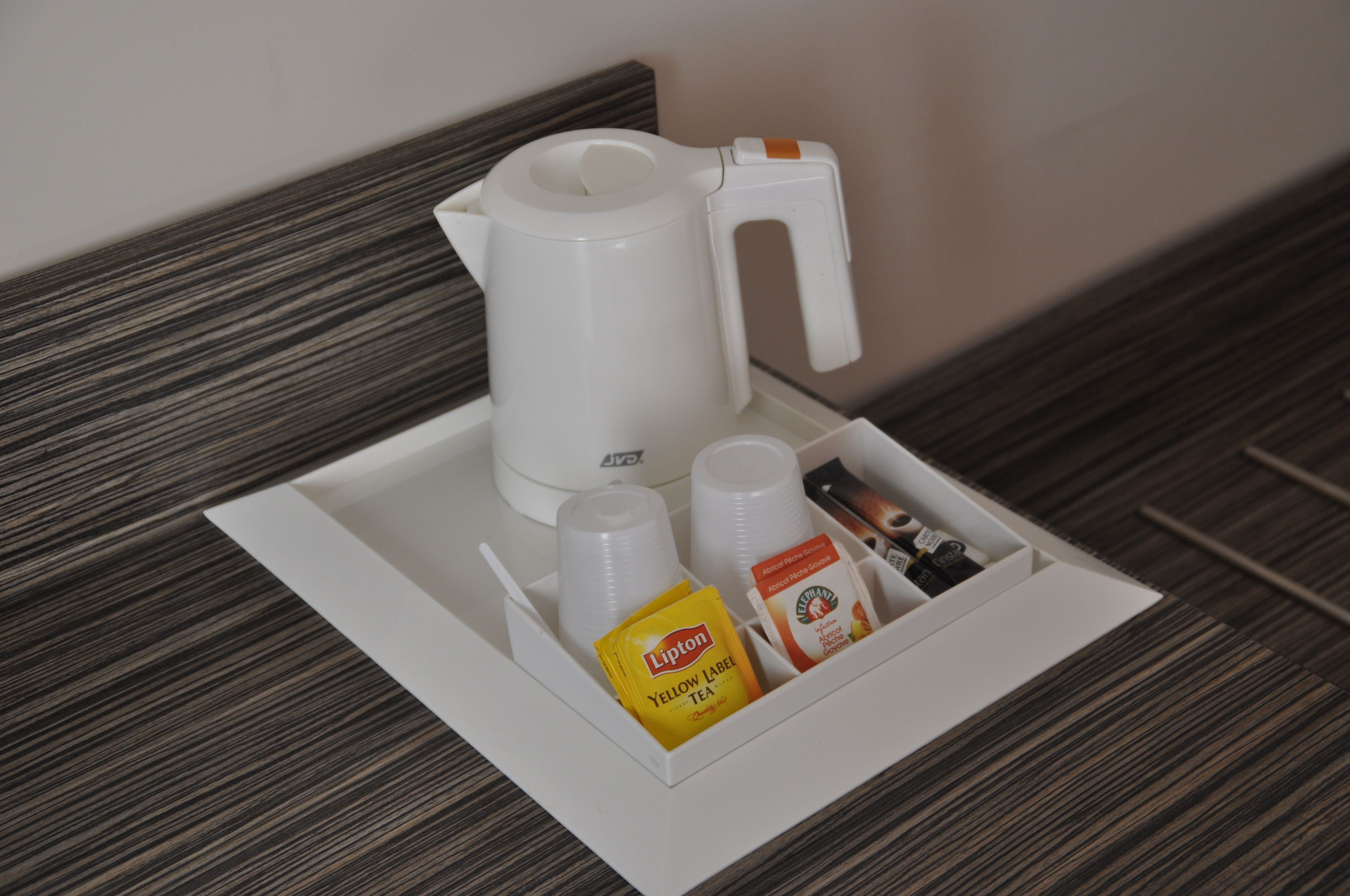 A hotel minibar with a white coffee maker, a yellow Lipton tea packet, and a box of tea bags.