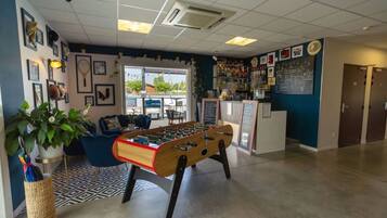 A room with a foosball table, a bar area with various bottles, and a seating area with a blue sofa and a potted plant.