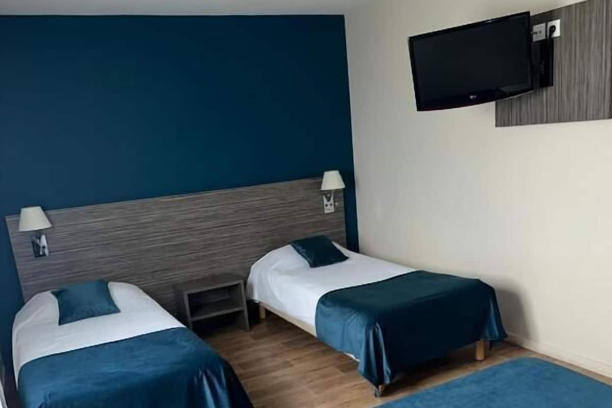 A hotel room with two single beds, a TV mounted on the wall, and a wooden headboard.