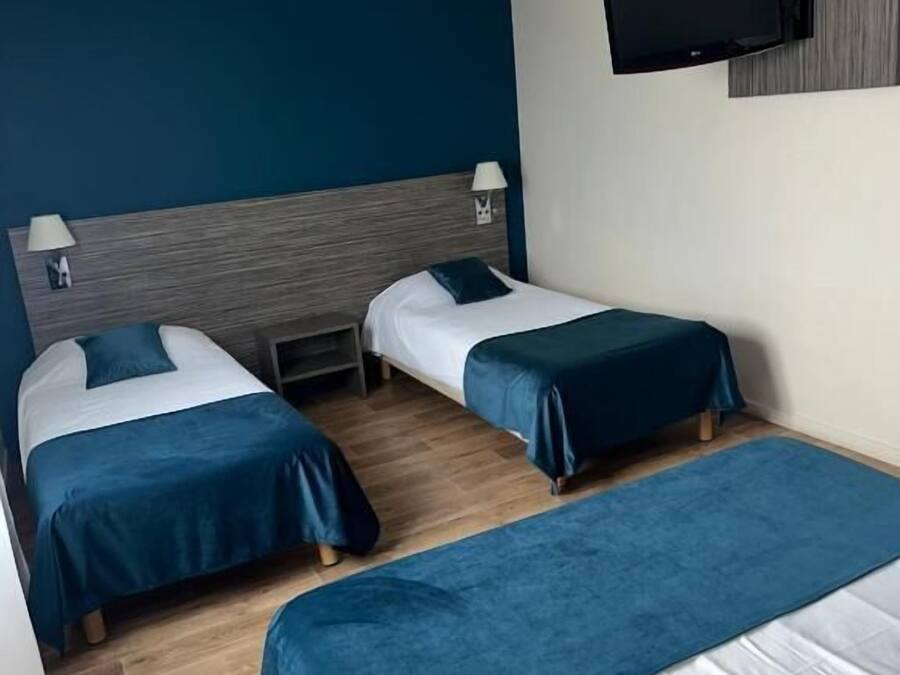 Ein Hotelzimmer mit zwei Einzelbetten, einem an der Wand befestigten Fernseher und einem hölzernen Kopfteil.