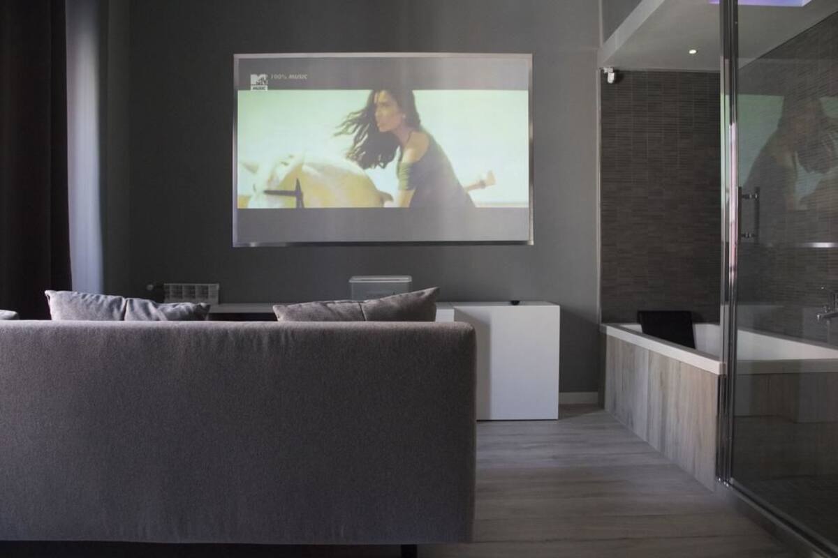 A modern living room with a large flat-screen TV mounted on the wall, a grey sofa, and a minimalist design.