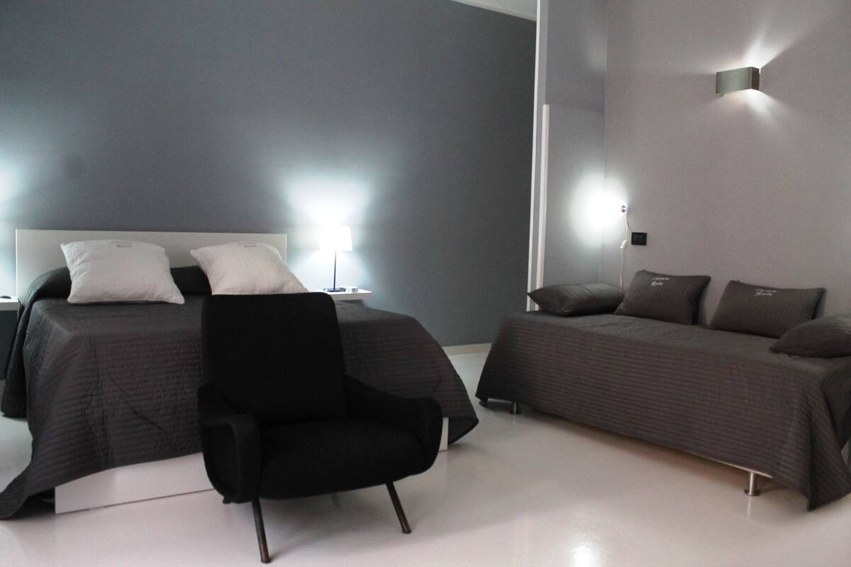A modern hotel room with a large bed, a smaller bed, and a black armchair.