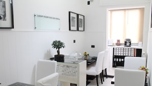 Un coin repas avec une table en verre, des chaises blanches, une plante en pot et un panneau indiquant qu’il s’agit d’une chambre de luxe.