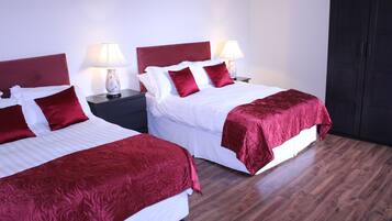 Two single beds with red headboards and white bedding, each with a bedside table and lamp. The room has wooden flooring and a dark wardrobe.