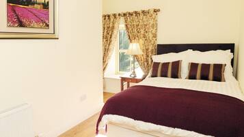 A bedroom with a bed, a nightstand, a lamp, a window with curtains, and a framed picture on the wall.