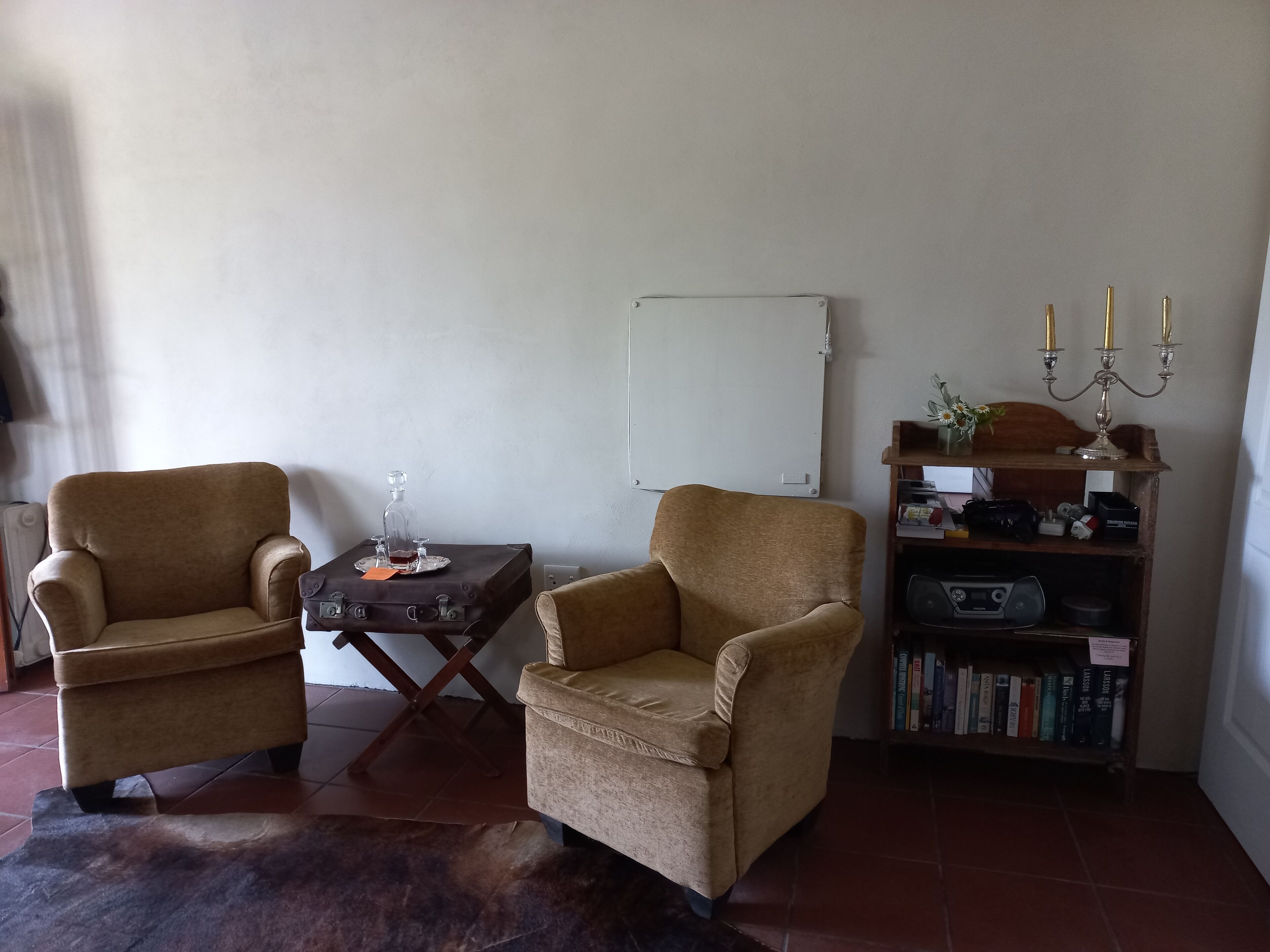 Una habitación con dos sillones, una mesita con una botella y un vaso, una pizarra, una estantería con libros y un candelabro.