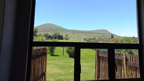 A view through a window of a rural landscape with hills, a wooden fence, and a clear sky.