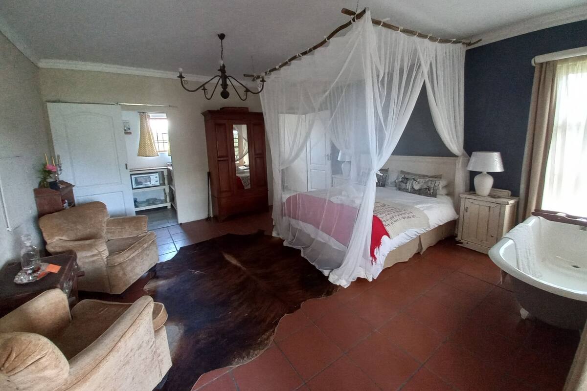 Quarto com cama de dossel, área de estar com cadeiras, banheiro com banheira e cozinha compacta ao fundo.