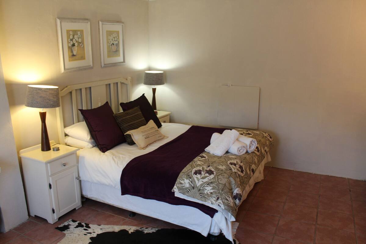 Cama bem arrumada com cabeceira, duas luminárias de cabeceira e uma mesinha de cabeceira com abajur.