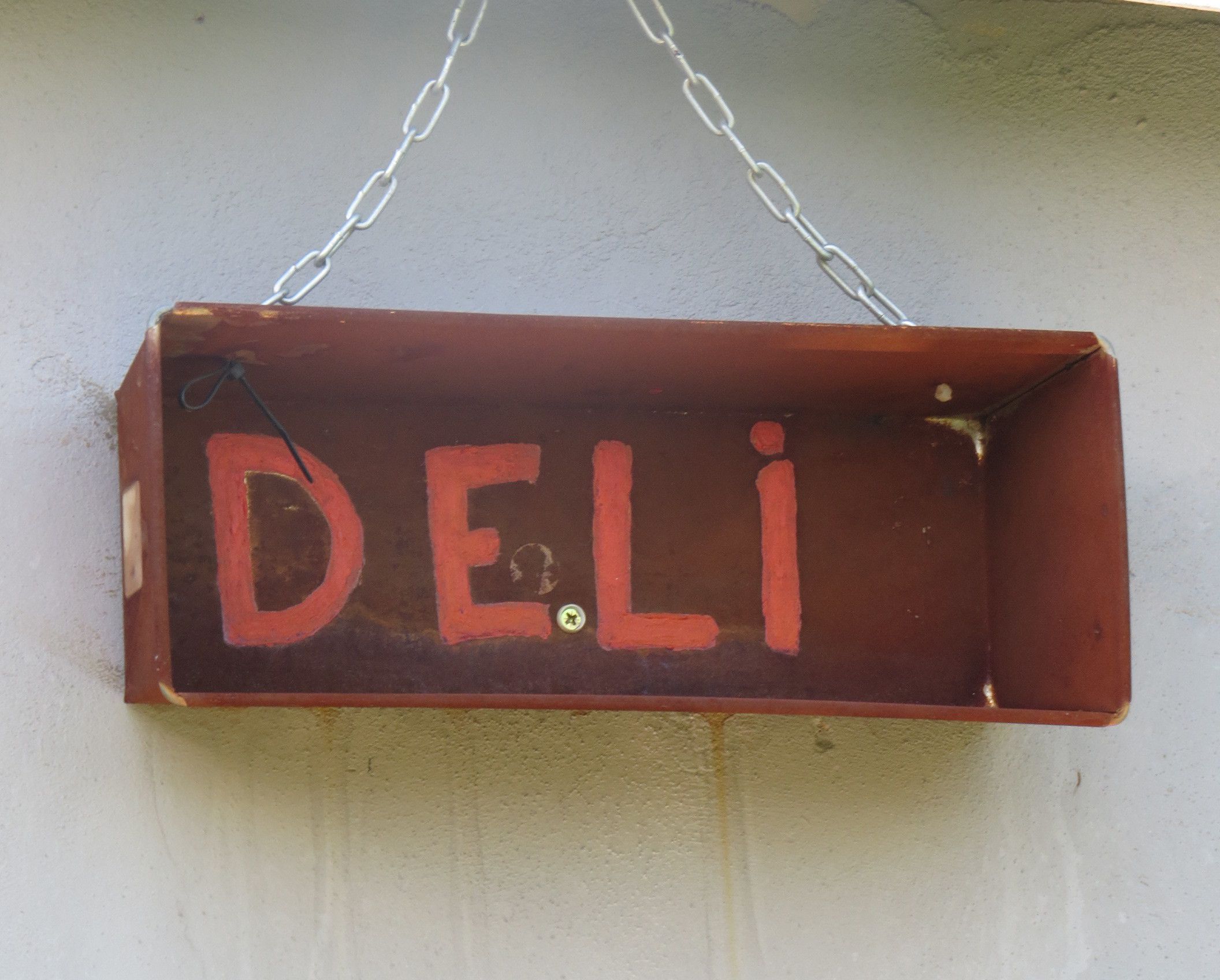 A wooden sign with the word "DELI" in red letters, hanging from a chain.