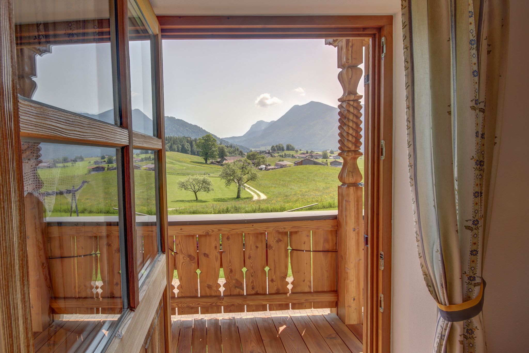 Un balcon en bois offrant une vue sur un paysage verdoyant et des montagnes.