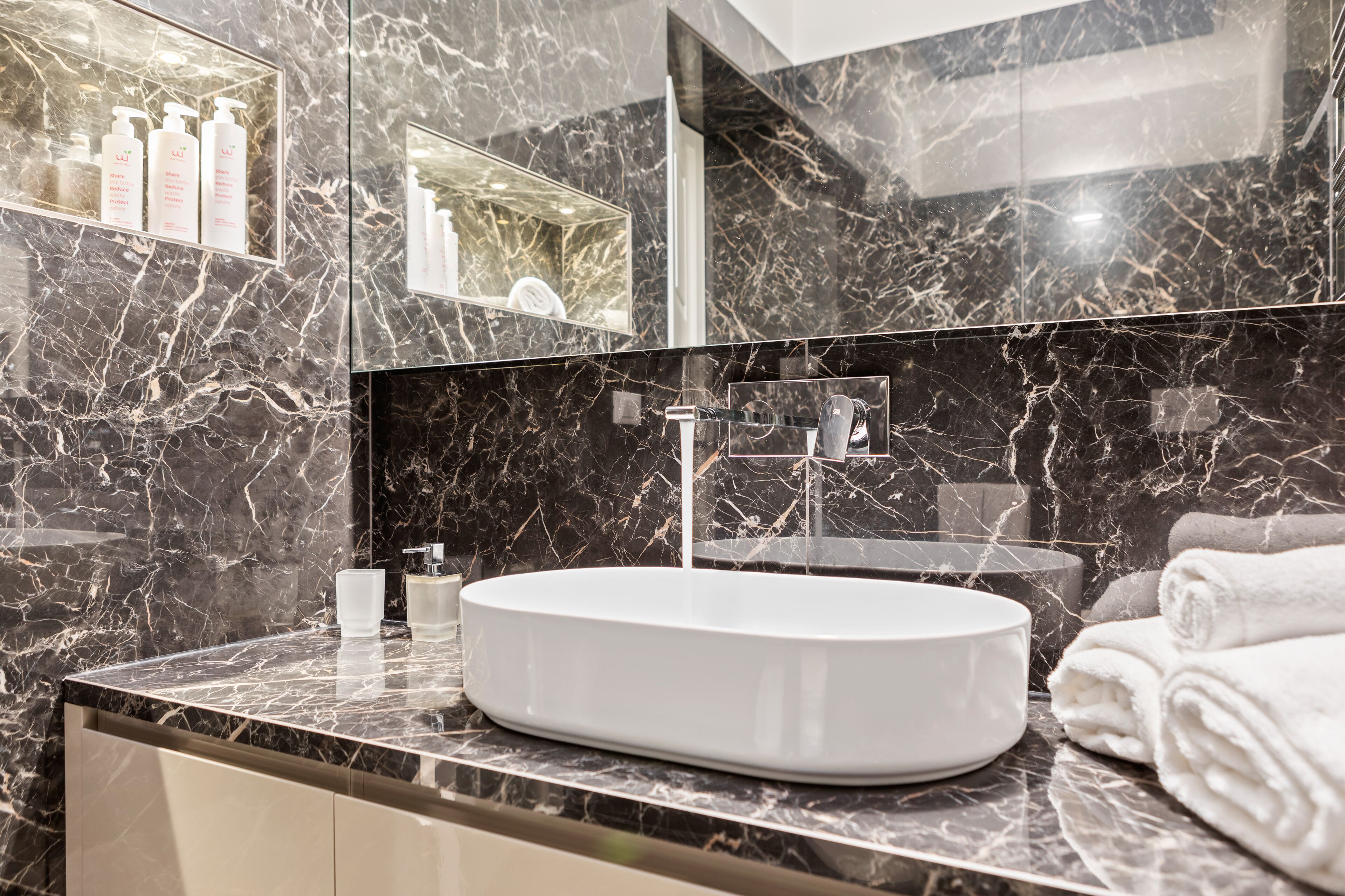 A modern bathroom with a marble vanity, a large mirror, and a built-in sink.