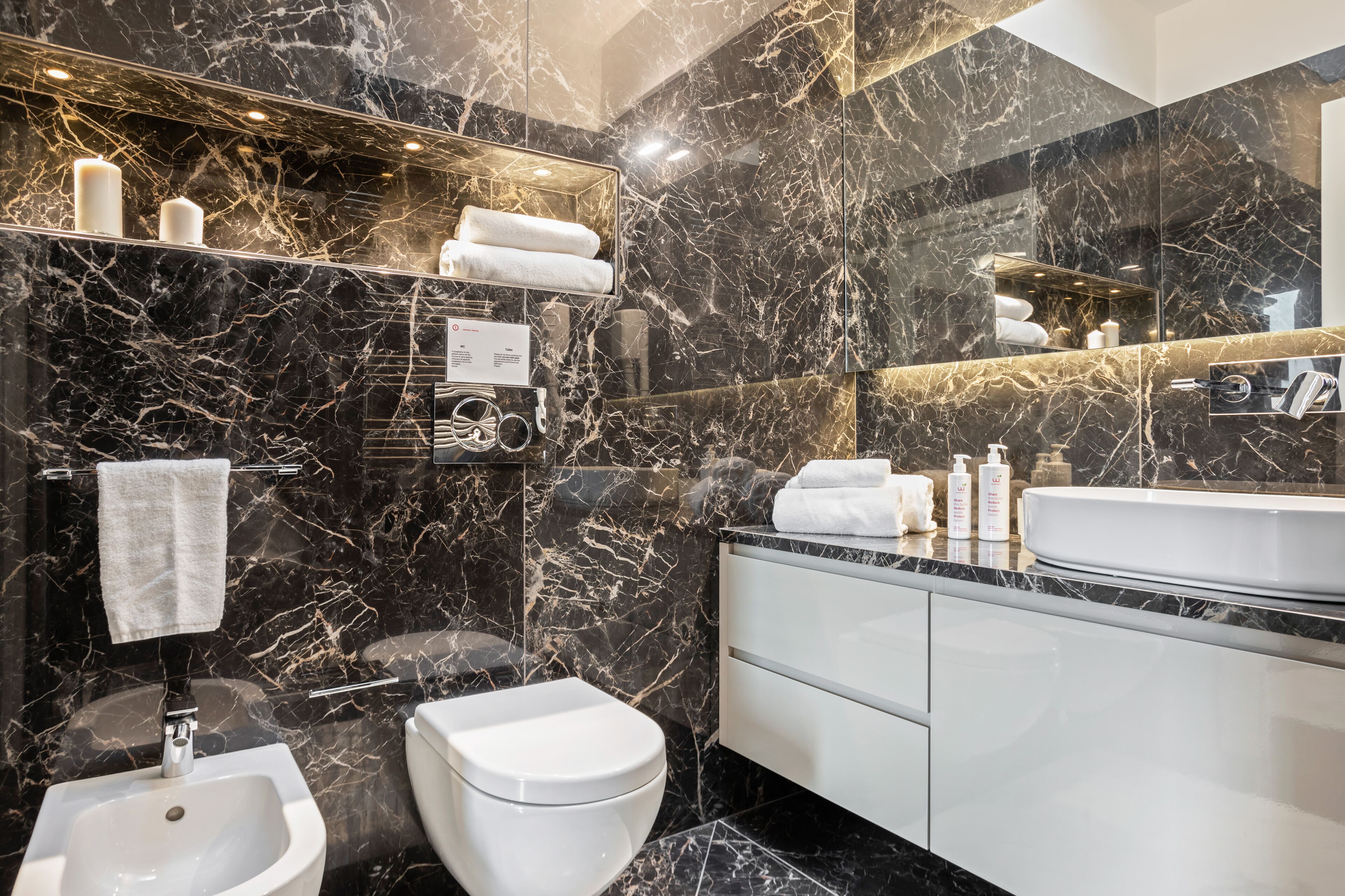 Un baño moderno con salpicadero de mármol, un lavamanos blanco y un bidé.