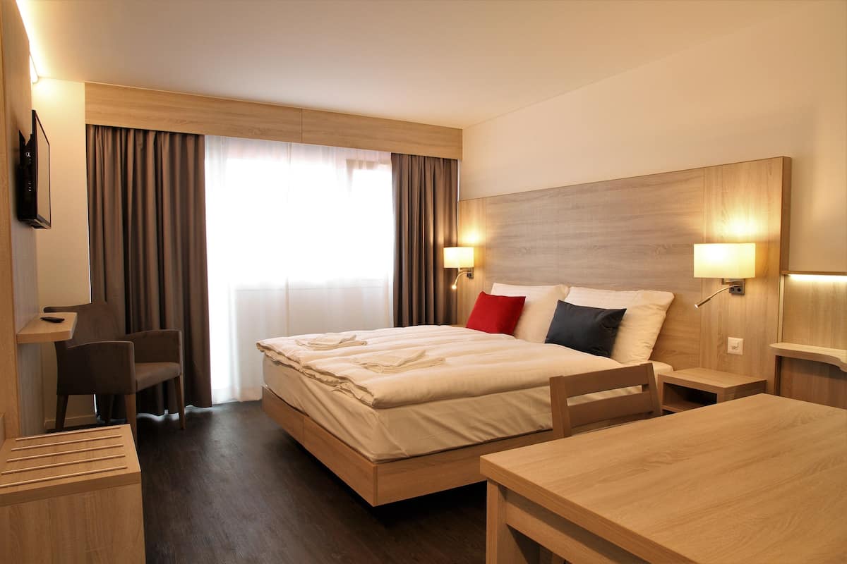 A hotel room with a bed, bedside tables, a desk, and a chair.