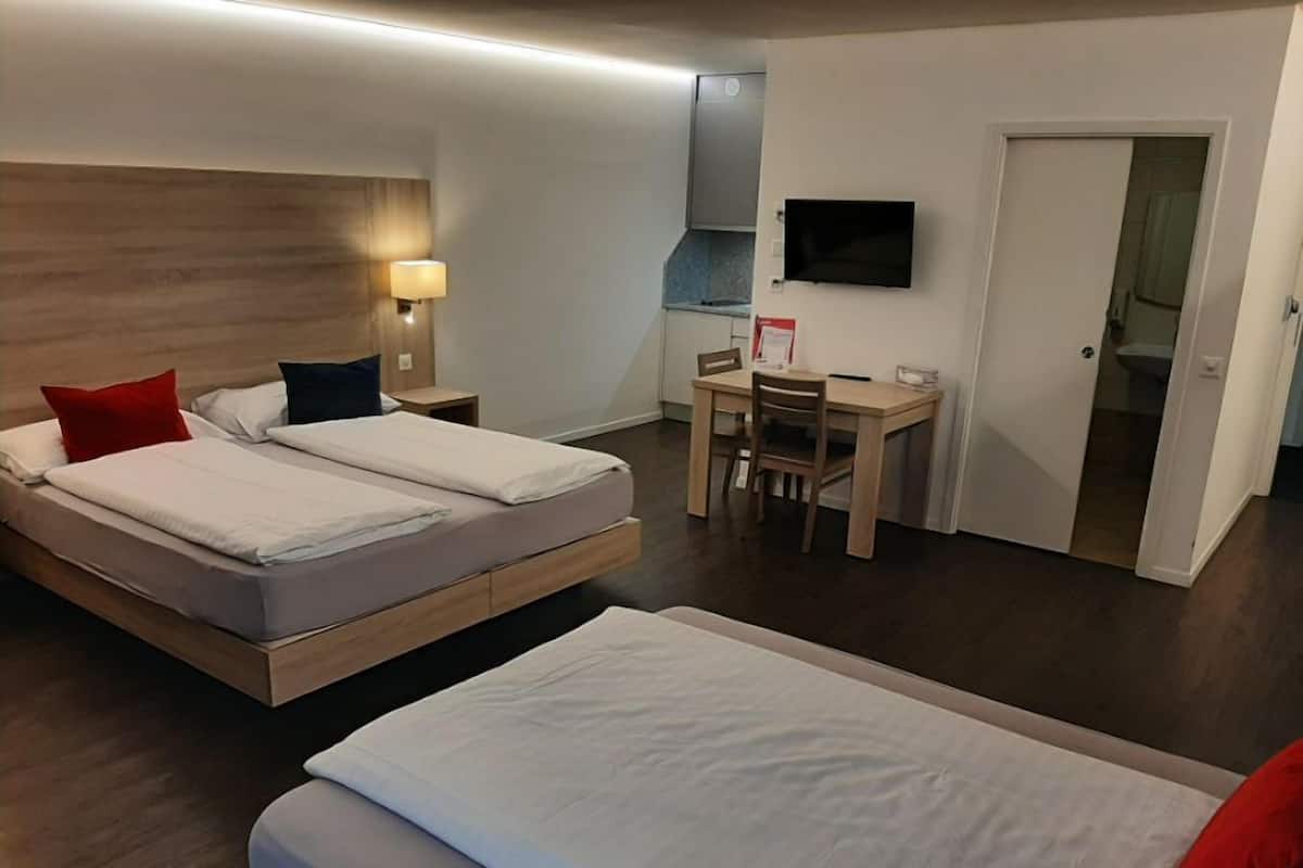 A hotel room with two beds, a desk, a chair, a TV, and a door leading to a bathroom.