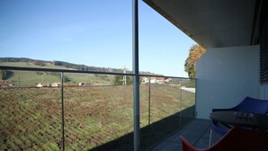 A balcony with a clear view of a green landscape and distant buildings. - Wego Hotel (Vuadens)